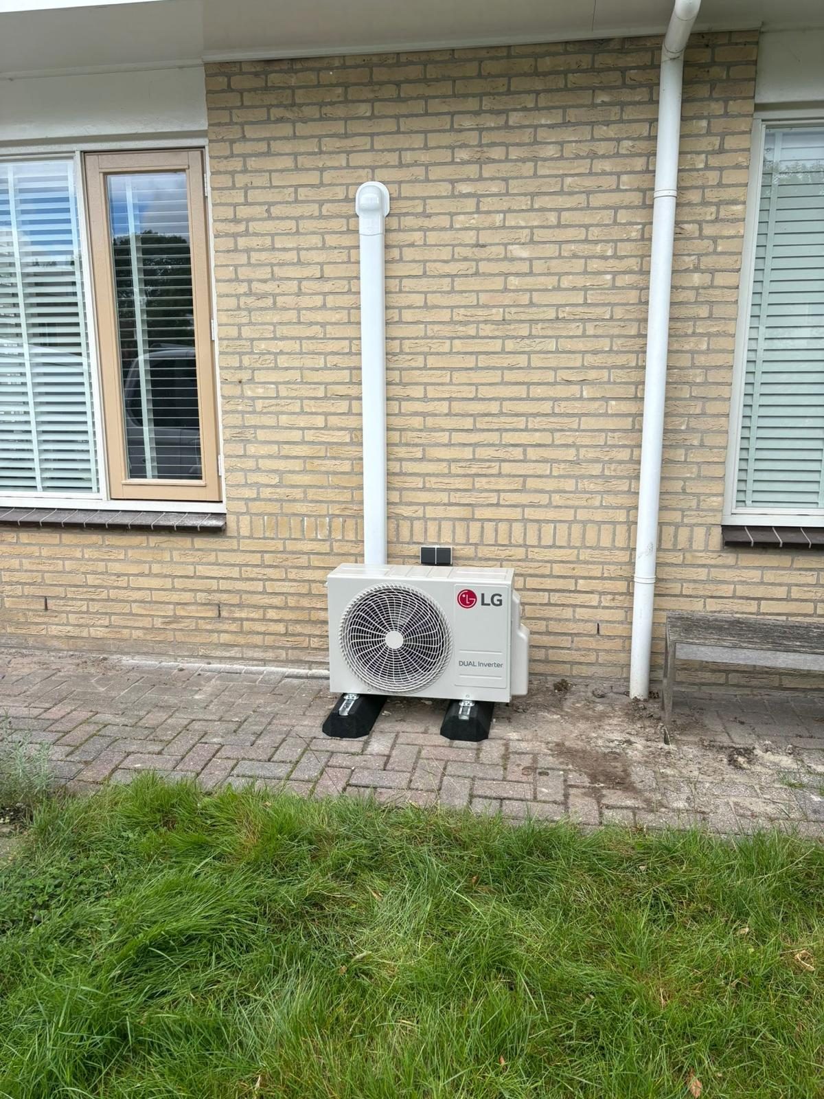 LG Dual Inverter buitenunit op rubberen voeten tegen een gevel in Roden, met witte leidinggoot naar boven