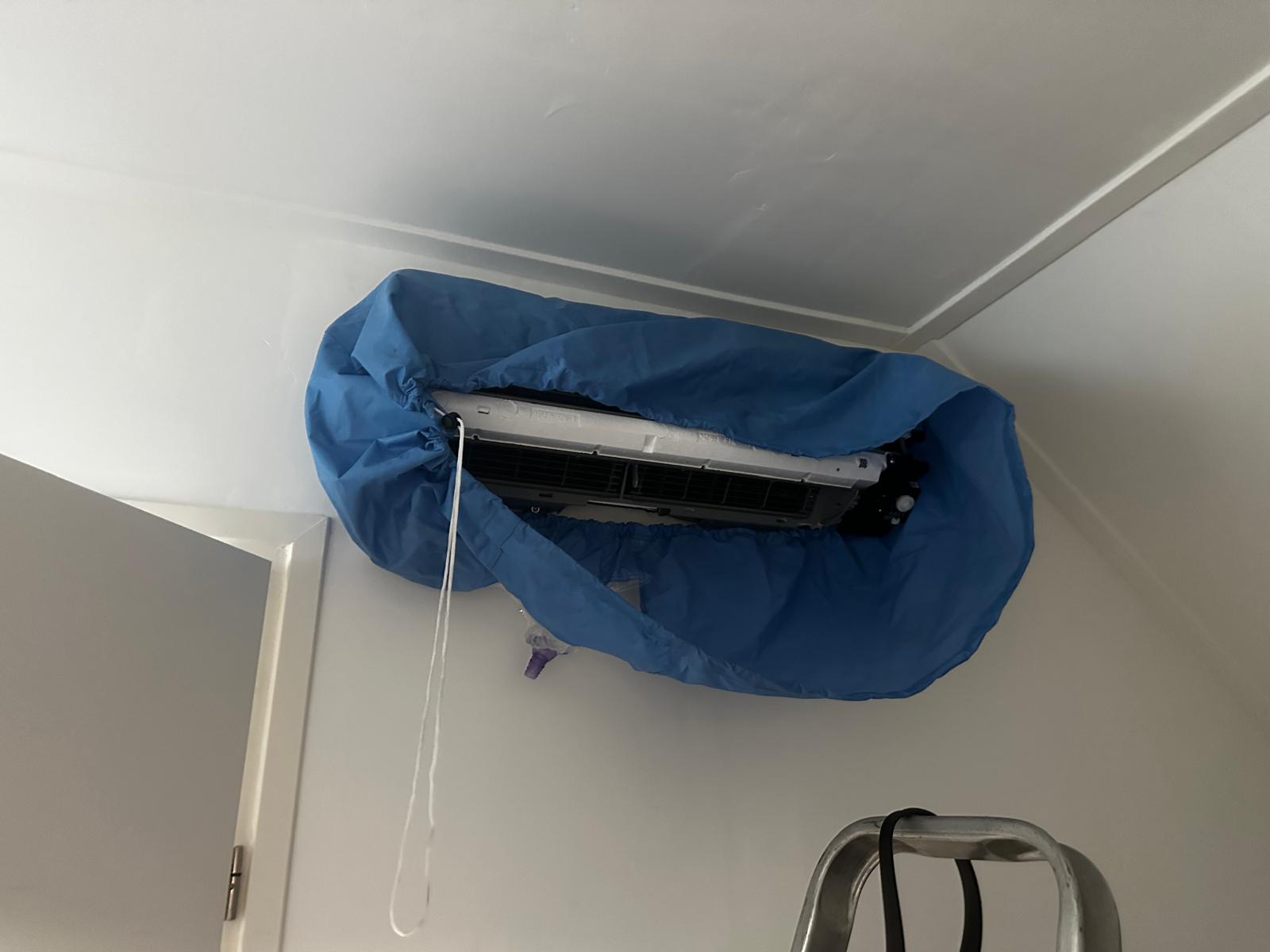 Daikin airco binnenunit afgedekt met een blauwe servicezak met afvoerslang, klaar voor een grondige reiniging